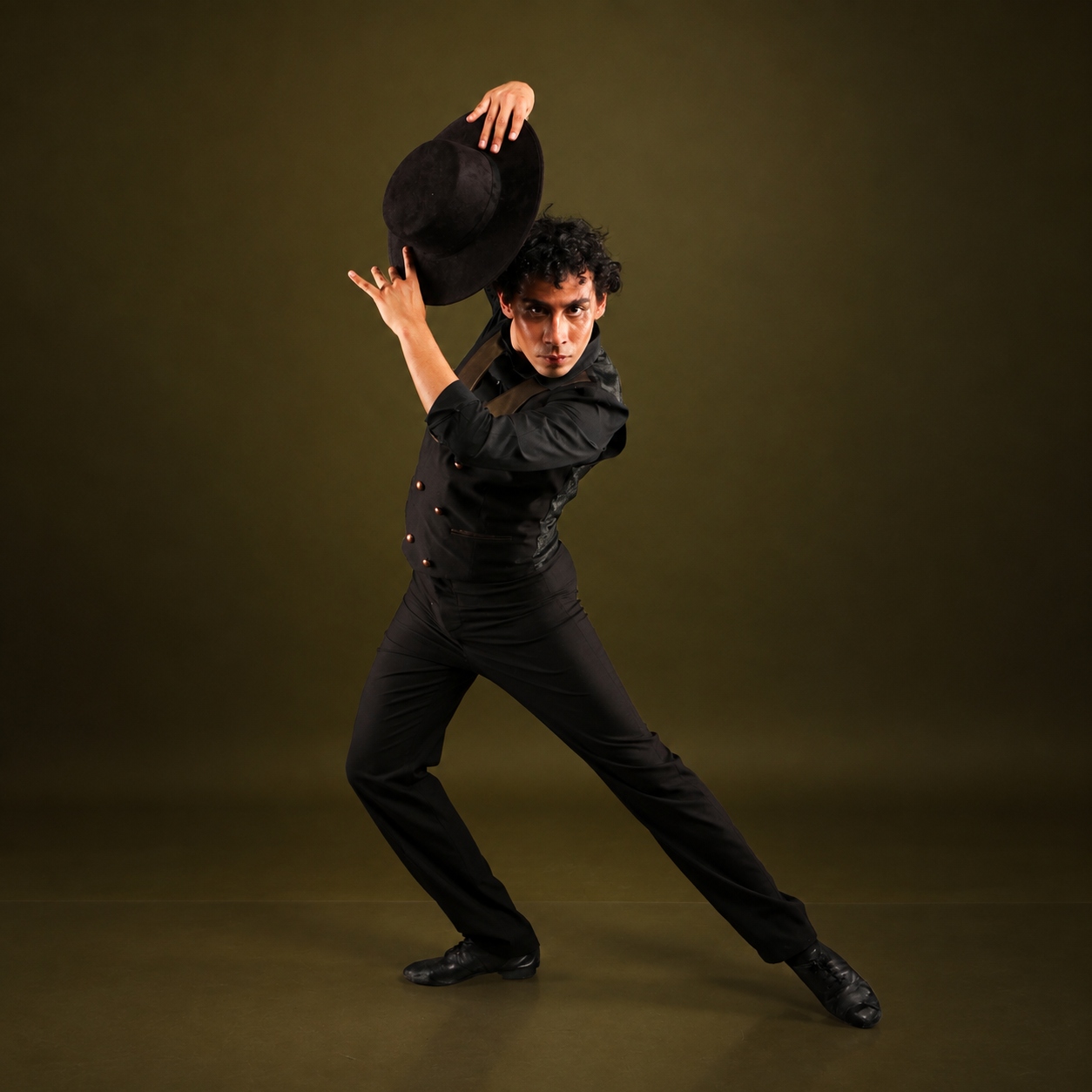 Dancer dressed in black holding a hat above his head in a dynamic pose