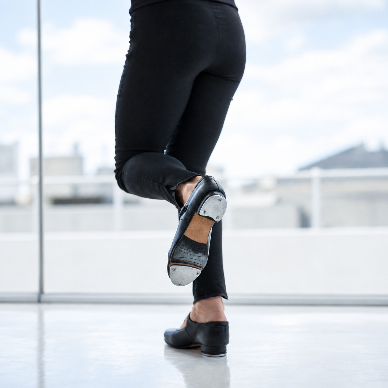 Tap dancer's foot in black tap shoes mid-step in a bright studio